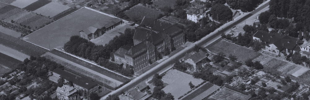 Ausschnitt aus einem Schrägluftbild von 1938. Das Gebäude der Samsonschule mit Schulhof. Neben der Turnhalle wurde eine Autogarage und Tankstelle für die mechanisierte Inantriedivision der Polizei errichtet.